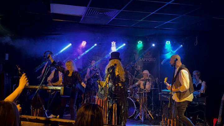 Fleetwood Mad musicians facing towards the drum kit beneath blue stage lights