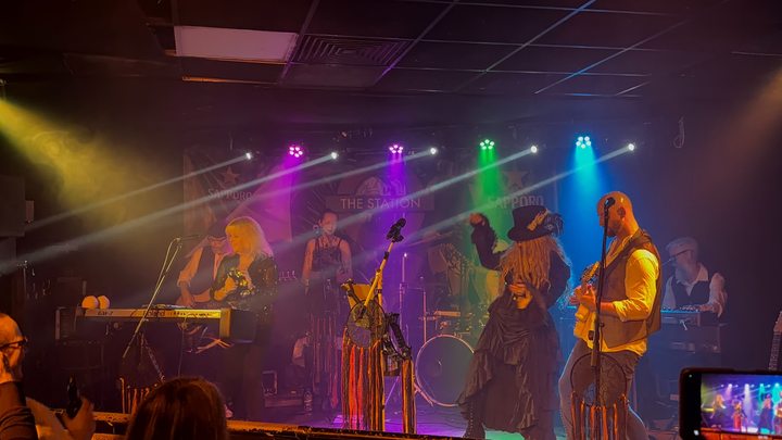 Fleetwood Mad keyboard player, singers, drummer and guitarist under multicoloured stage lighting