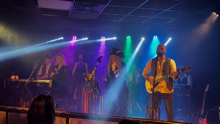 Fleetwood Mad guitarist and singers performing beneath blue, pink and green stage lights