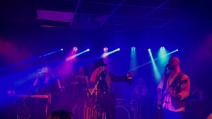 Fleetwood Mad performing under purple and blue lighting with singers at centre stage