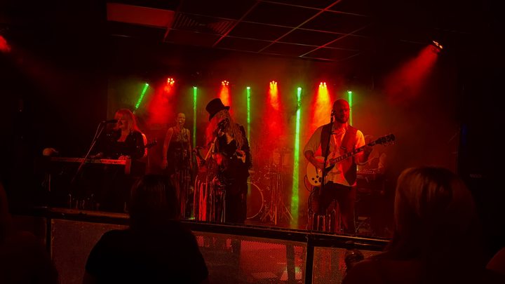Fleetwood Mad on stage beneath red and green lights with audience silhouettes in front
