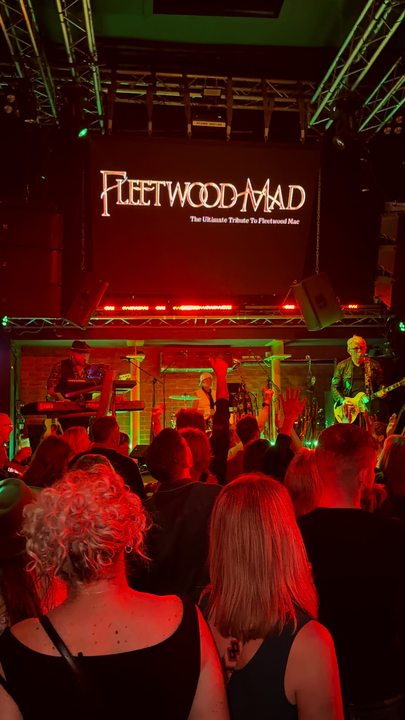 Audience watching Fleetwood Mad beneath a large screen displaying the band name
